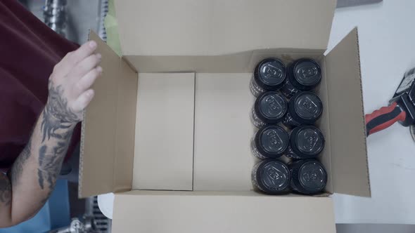 Top View Of Tattoed Worker Packing Canned Beers In A Box In A Beer Factory
