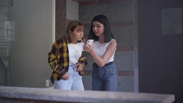 Portrait of Angry Teenage Girl Threatening Classmate Showing Social Media on Smartphone