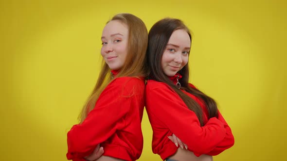 Two Slim Young Women Posing Back to Back Smiling Standing at Yellow Background