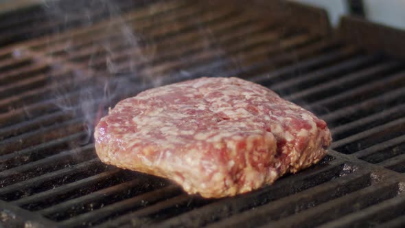 Slow motion of beef hamburger on a grill in close up with flames and smoke