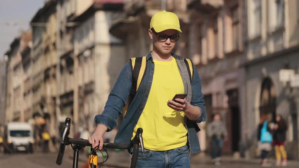 Portrait of a Young Delivery Man Who is Going and Holding a Smartphone