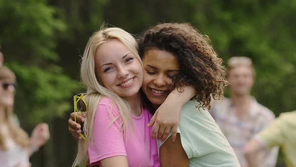 Positive Female Couple in Love Hugging Cheek to Cheek, Looking Into Cam at Party