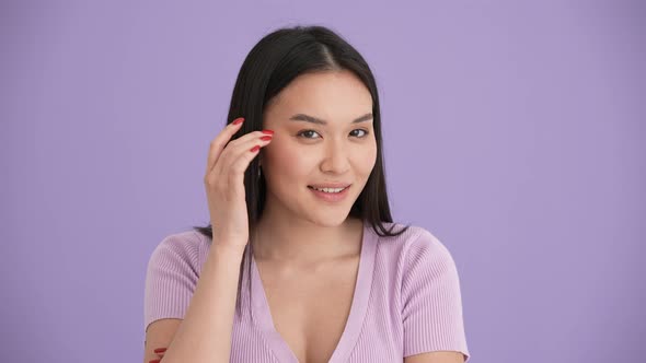 Happy Asian brunette woman wearing purple t-shirt twirling hair around finger