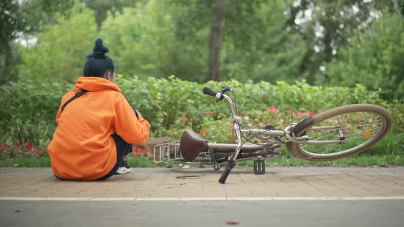 Wide Shot Back View of Millennial Caucasian Woman with Injured Leg Sitting on Park Alley with