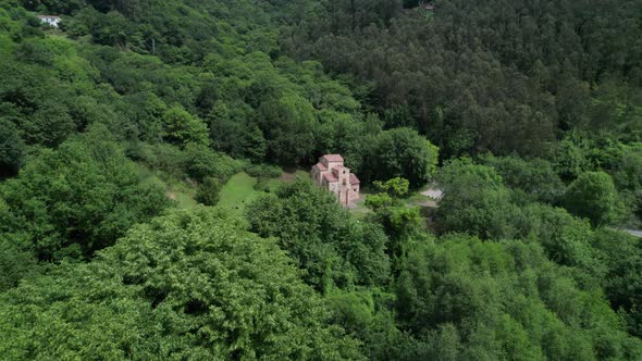 Droone flying towards ancient and roman church in green natural forest environment