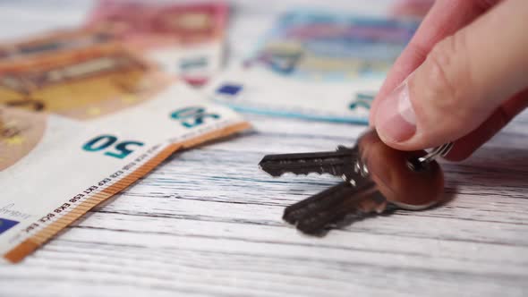 The keys to the apartment or house, the hand lays on a white wooden table with euro banknotes