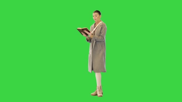 Young Woman in Grey Coat Stands Reading a Book on a Green Screen Chroma Key