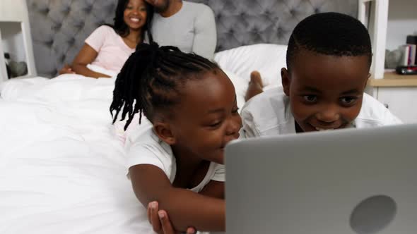 Children using laptop while couple smiling in background