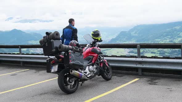 Biker on Tourist Motorbike with Luggage Bags Stands By Mountain Landscape Alps