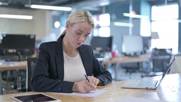 Serious Businesswoman Writing on Papers While Working in Office