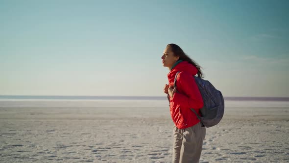 Slow Motion Walking Woman in Red Jacket and Backpack on White Salt Beach