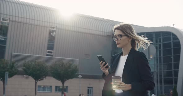 Stylish Girl in Suit walking down the street, texting Messages on Smartphone.