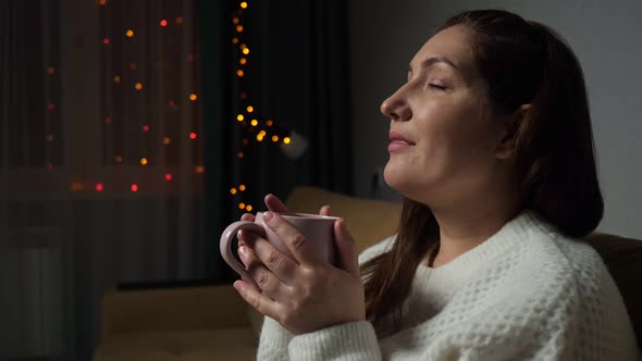 Brunette Lady Drinks Hot Coffee Sitting on Sofa at Christmas