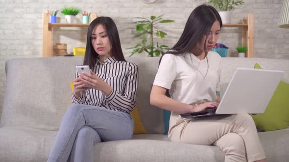 Two Young Asian Women Are Using Gadgets Sitting on the Sofa