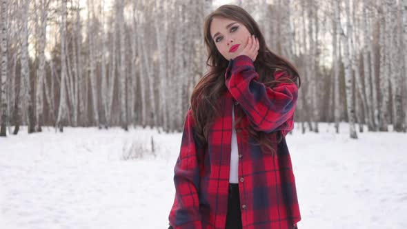 Young Woman with Wavy Hair Standing and Touching Face in Winter Forest