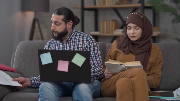 Busy Overworking Middle Eastern Man Analyzing Idea Online As Relaxed Woman Reading Book Sitting on