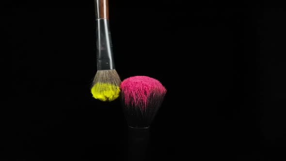 Makeup Brushes Touch Each Other on Black Dark Background and Small Particles of Color Cosmetics