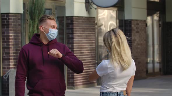 Portrait of Young Man and Woman Greet Each Other in the Street with Elbow Touches and Communicate