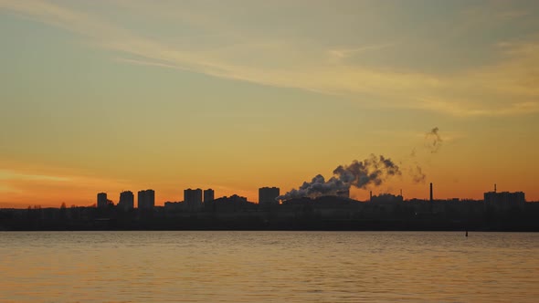 An Industrial District Behind a River During Sunset