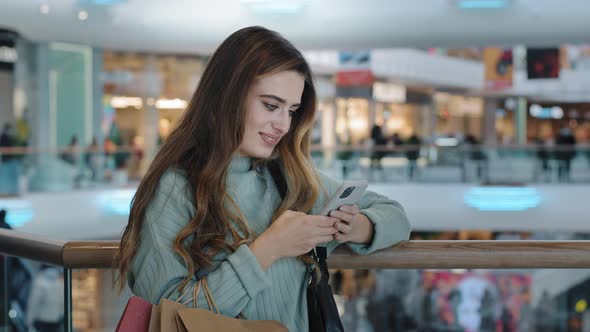 Woman Consumer Female Shopaholic Girl Standing in Shopping Center with Packages Looking in Mobile