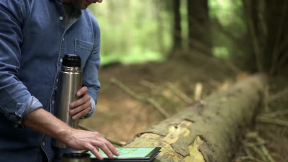 Hiker drinking coffee and using tablet in the forest