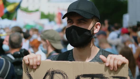 Political rally riot activist in face mask with poster sign against coronavirus.