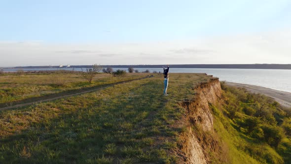 Tracking Aerial Shot of Young Woman Enjoying Sunset in Field and Running Near the Cliff During