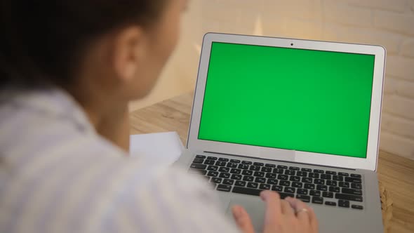 The girl is working at a laptop with a green screen