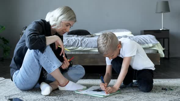 A Young Mother and a Baby Boy Are sitting on the Floor, The Boy Is Drawing with Felt-Tip Pens