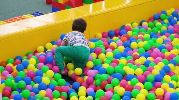 A Little Boy Crawls in a Pool with Soft Plastic Balls in the Playroom