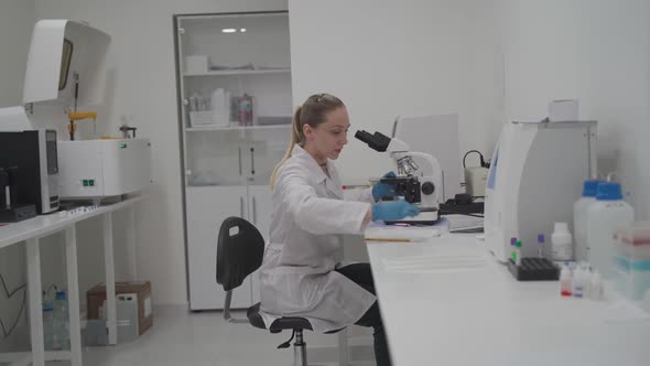 Female Medical Professional Works with Samples and Analyzes in Medical Laboratory Behind Microscope