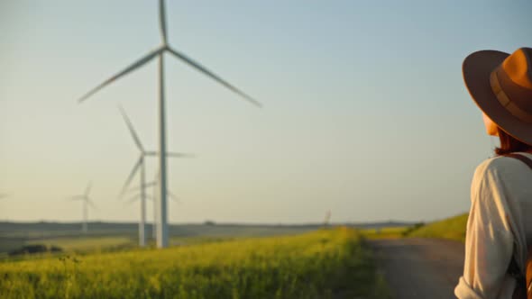 Young tourist in a hat looking at eco windmills in a field