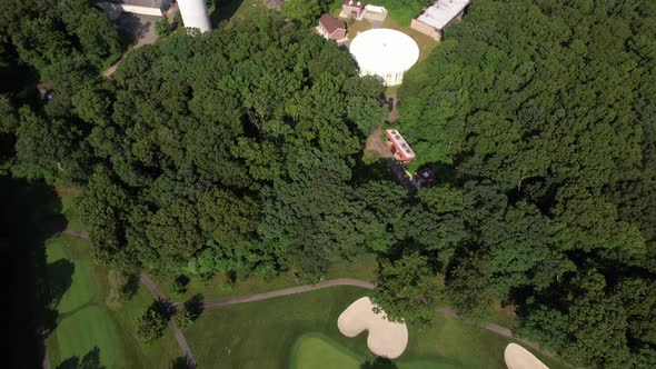 A top down drone view over a golf course, then tilt up to reveal water towers in a suburban neighbor