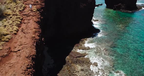 Drone shots of a cliff side beach with blue waters and no one around but 1 man running on the cliffs