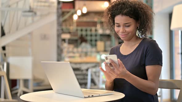 Smartphone Use By Young African Woman with Laptop in Cafe 