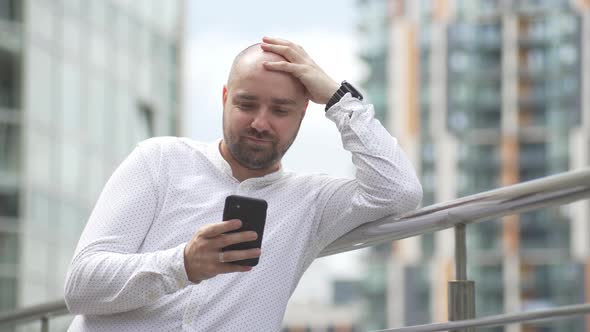 A Male Businessman in an Urban Landscape is Texting on the Phone and Smiling