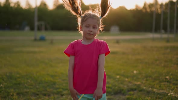 Pretty Little Girl Shakes Ponytails Standing on Park Meadow