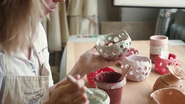 Close Up View of Female Potter Wearing Apron Using Glaze Brush to Paint on Pot