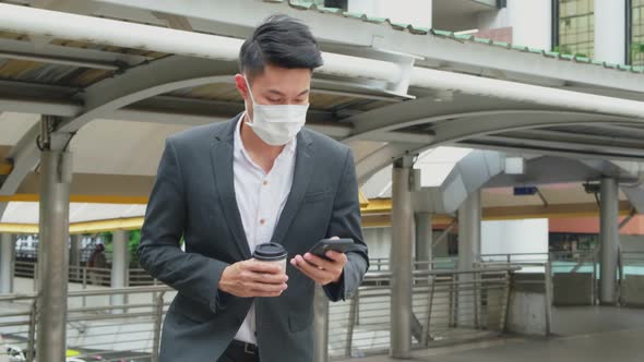 Asian young businessman wear face mask and walking up on stair going to work and use mobile phone.