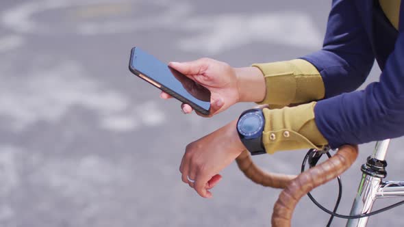 African american woman using smartphone in street leaning on bicycle