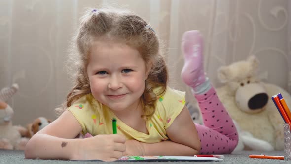 Curly blonde four-year-old girl draws with a felt-tip pen on a piece of paper.