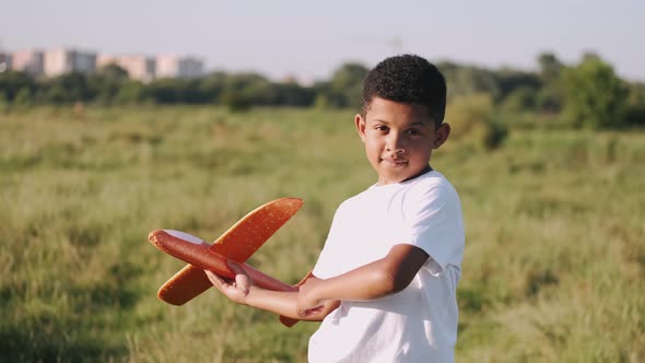 African Boy in a White Shirt with a Plane in Hands on Field