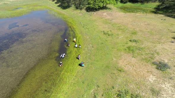 Aerial footage of a small group of refugees slowly wading through a pond.