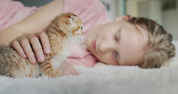 The Girl Lies on the Floor in the House Next to Her is Her Pet  a Red Kitten