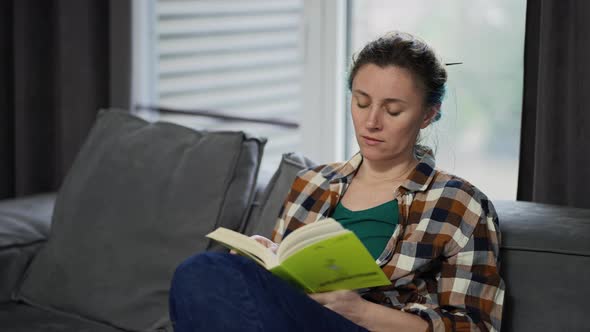 Young Pretty Woman Reading Book While Sitting on Sofa at Home