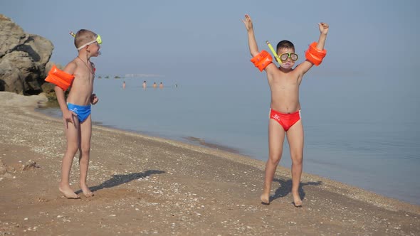 Family Vacation at the Sea. Boys on a Sandy Beach in Diving Masks and Life-saving Armbands Jump Up.