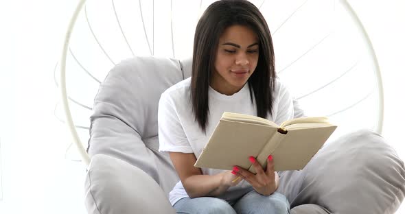 Young black woman reading interesting developing book at home.