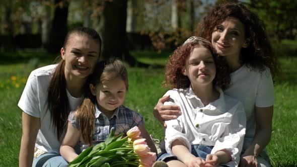 Two Women with Their Daughters are Sitting in the Park on the Grass