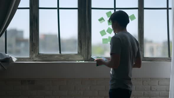 Silhouette of Young Asian Man Entering Home Office with Tablet and Looking Out the Window on Sunny