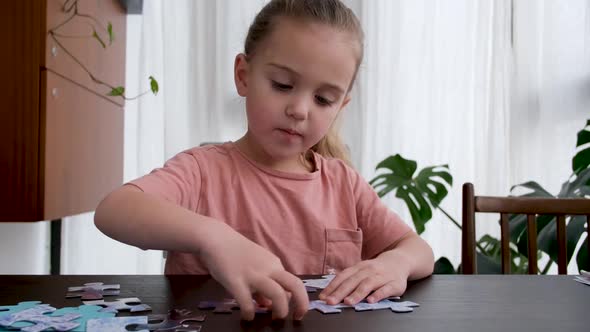Blonde Little Girl Does Jigsaw Puzzles Sitting at Table